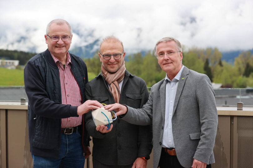 3 Menschen auf einer Terrasse, die auf einen Pokal greifen.