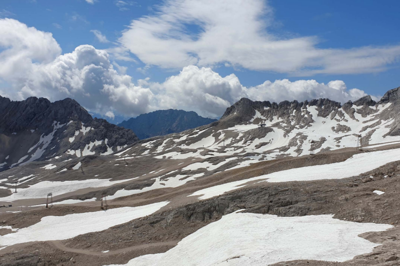 Aussicht auf Berge, die leicht Schneebedeckt sind mit blauem, wolkigem Himmel.