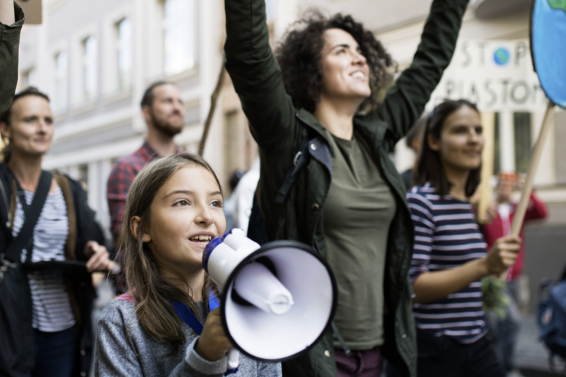 Junge Menschen mit Plakaten auf einer Demonstration. Ein Mädchen hält ein Megaphon.