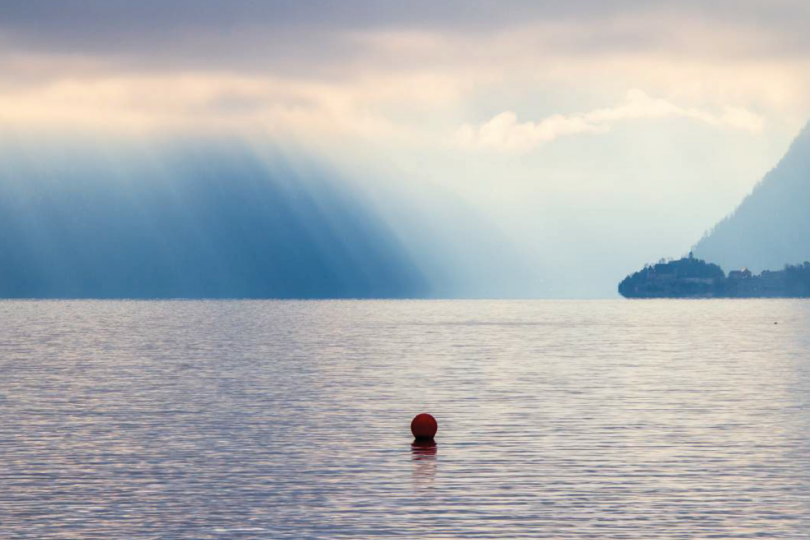 See mit Regenwolken im Hintergrund und einem schwimmenden roten Ball auf der Oberfläche.