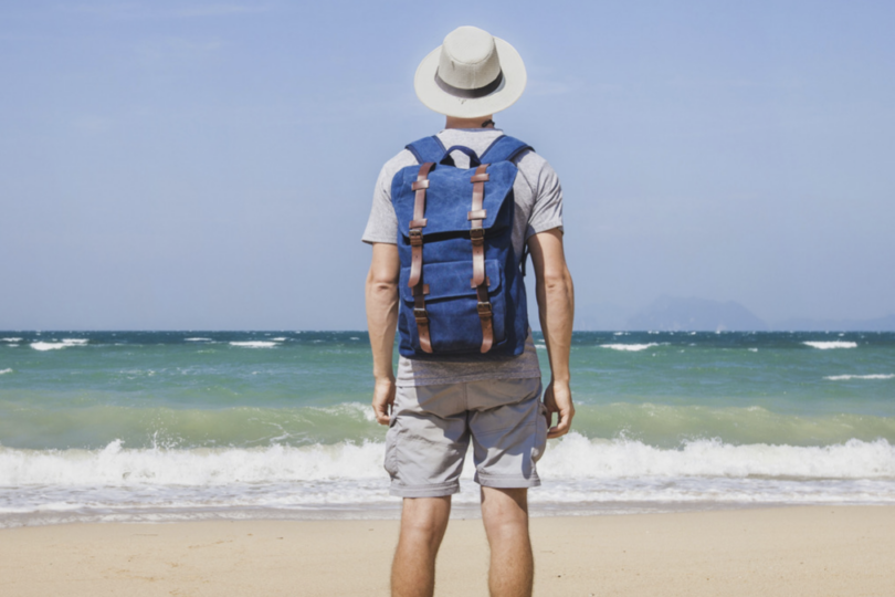 Mann mit Rucksack am Sandstrand, der aufs Meer blickt.