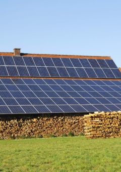 Auf dem Bild ist ein Bauernhaus zu sehen, welches eine große PV-Anlage auf dem Dach hat. Die PV-Dachanlage dient auch als Überdeckung für Brennholz.