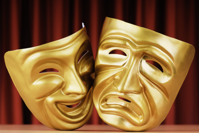 Goldene Theatermasken vor rotem Vorhang.