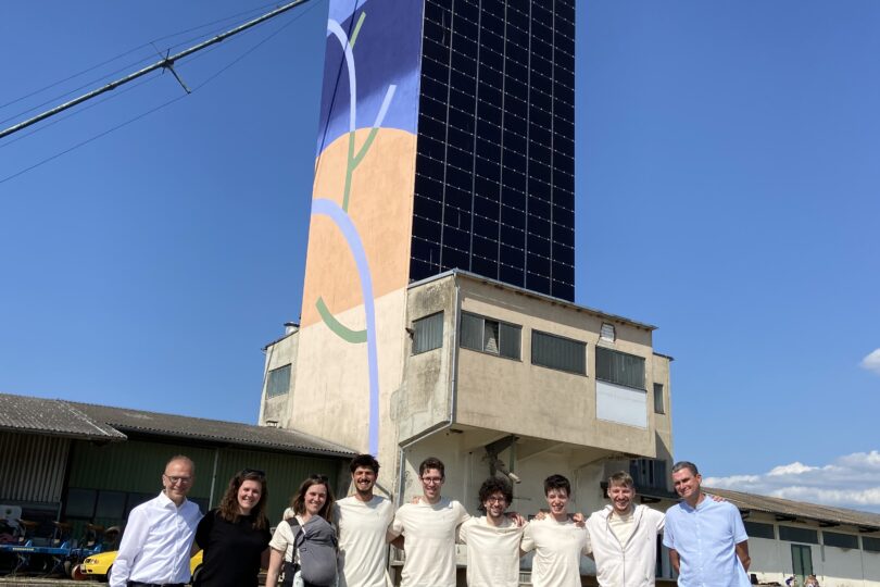 Das Bild zeigt Bernd Vogl, den Geschäftsführer des Klima- und Energiefonds, zusammen mit dem Team des Projektes „Solar Silo“. Im Hintergrund ist der Solar Silo Turm zu sehen, der teilweise mit einer Solar-Paneel-Fassade und einer abstrakten, farbenfrohen Wandgestaltung versehen ist. Die Gruppe steht bei sonnigem Wetter vor dem Turm und lächelt in die Kamera, um die erfolgreiche Eröffnung dieses innovativen Projekts zu feiern.