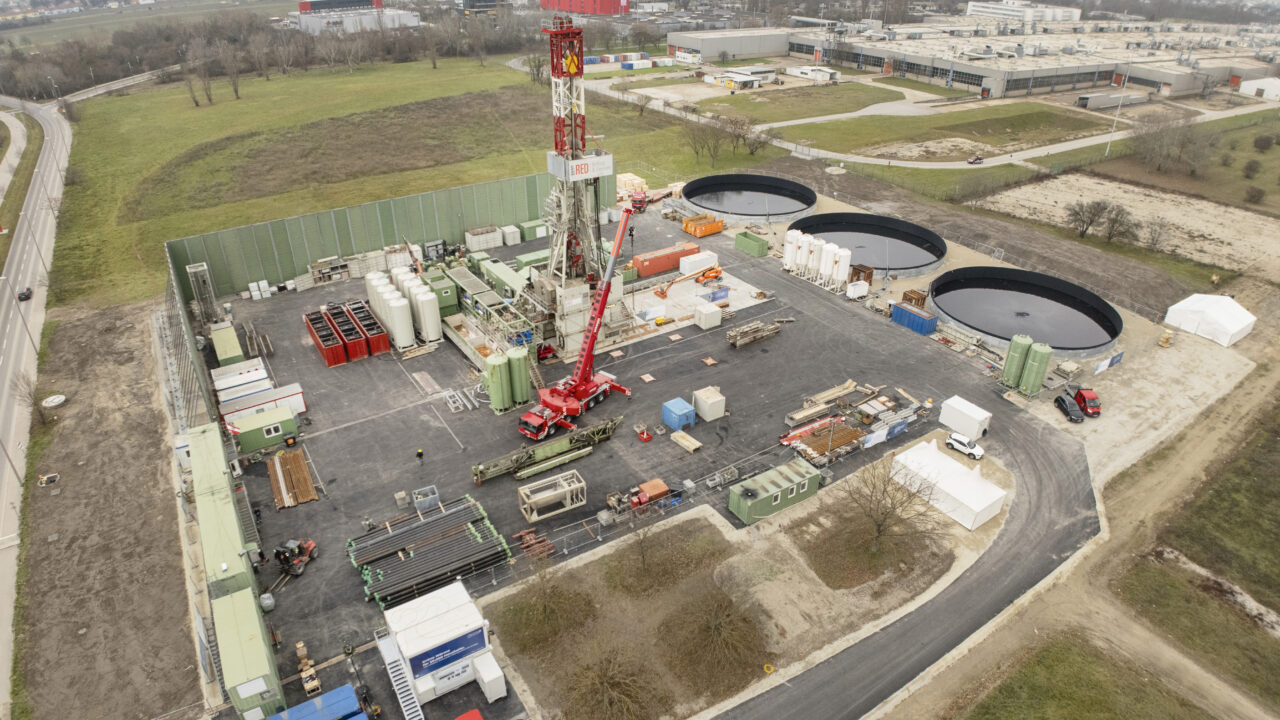 Man sieht einen Bohrturm, runde Wasserbecken und industrielles Gelände