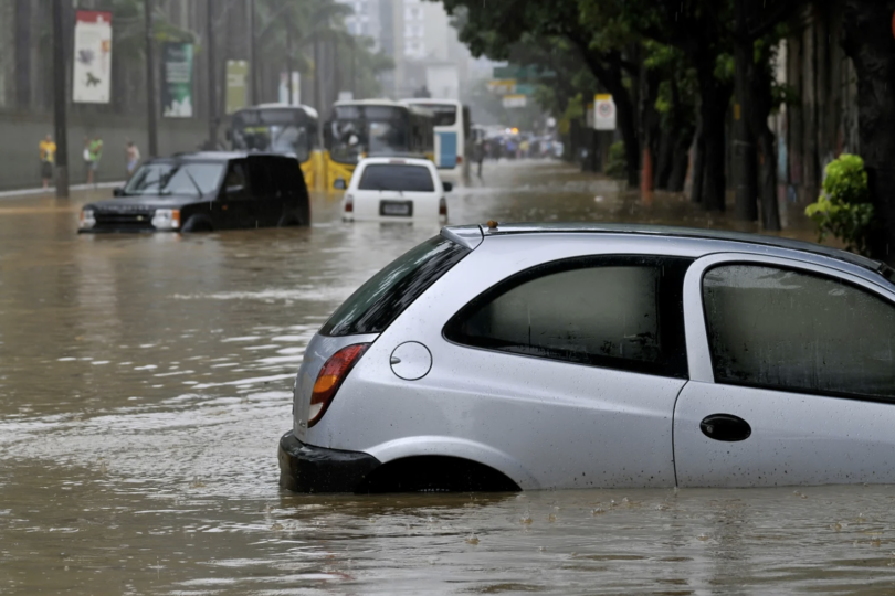 Eine überschwemmte Straße mit teilweise überfluteten Autos, die starke Regenfälle und städtische Überschwemmungen inmitten eines bedrohlich grauen Himmels verdeutlicht.